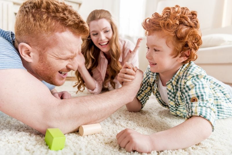 Father and son playfully arm wrestle as mom looks on