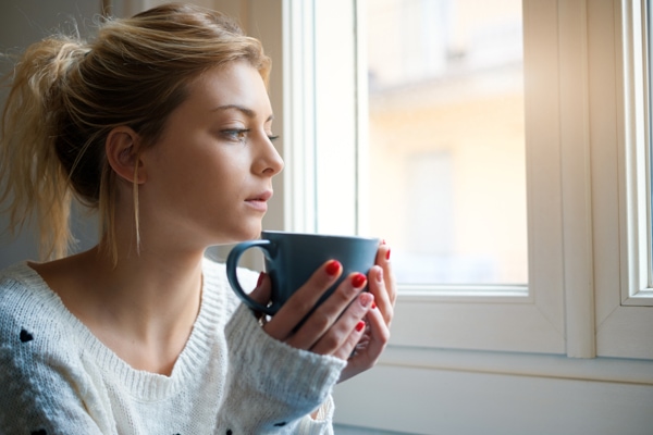 woman looking out window with coffee mug