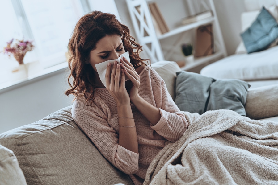 Top view of sick young women blowing her nose using facial tissues while sitting on the sofa at home. How UV Lights Benefit Your HVAC System