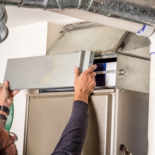 Man removes the furnace filters cover to inspect