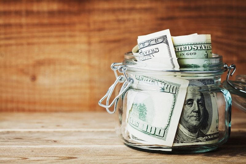 Dollar bills in glass jar on wooden background. Saving money on heating bill concept.