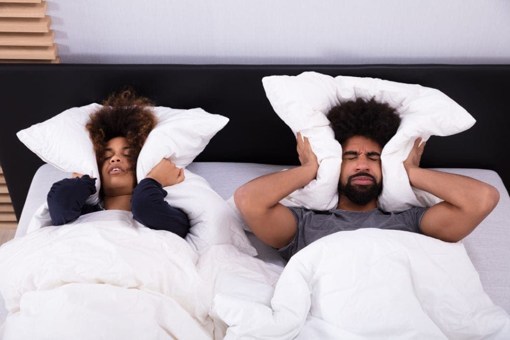 Young Couple Covering Their Ears With Pillow From Loud Furnace Noise.